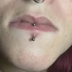 Labret co to? Kolczyk w wardze i pod nią, ozdobiony metalowymi kulkami. Skóra z piegami.