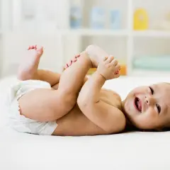 Bambino sorridente in pannolino gioca con i piedini, felice dopo aver fatto la cacca neonato.