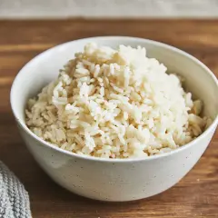 Eine Schüssel mit gekochtem parboiled Reis steht auf einem Holztisch. Der Reis ist locker und hat eine helle Farbe.