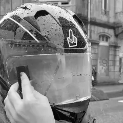 Mano colocando el Pinlock en un casco de moto mojado por la lluvia, listo para instalar.