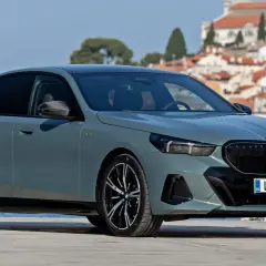 Eleganckie, szare BMW 520 z czarnymi felgami stoi na tle malowniczego, nadmorskiego miasteczka.