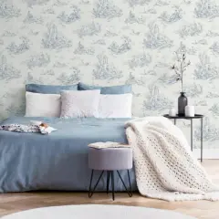 Chambre paisible avec un papier peint au motif jouy bleu et blanc, un lit bleu, des coussins blancs et une couverture en maille.