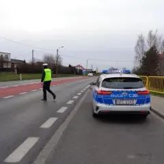 Policjant w kamizelce odblaskowej kieruje ruchem obok radiowozu. Może to być kontrola drogowa lub reakcja na wykroczenie 97 kw.