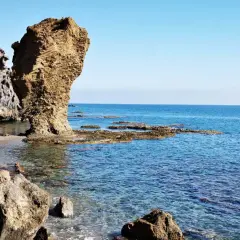 Rocas erosionadas y mar azul en la playa El Sombrerico. Una formación rocosa alta se alza como un guardián.