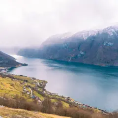 Malownicze fiordy Norwegii z ośnieżonymi szczytami gór, zielonymi zboczami i malowniczą wioską nad wodą.