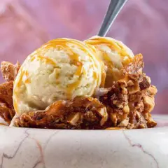 Zwei Kugeln cremiges Eis mit Honig statt Zucker, garniert mit karamellisierten Nüssen und einem Löffel.