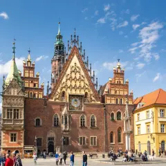 Stary Rynek we Wrocławiu tętni życiem. Wspaniały Ratusz z zegarem astronomicznym dominuje nad placem, gdzie spacerują ludzie.