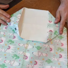 Mani che piegano carta regalo con lama e cactus per creare mini sacchetti di carta fai da te.