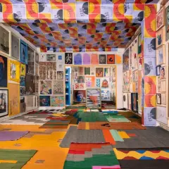 Vibrant art fills a room, from the ceiling posters to the floor rugs, showcasing the diverse creativity of Mexico City Art Week.