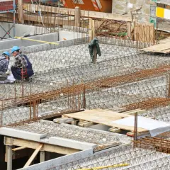 Bauarbeiter prüfen Pläne für verschiedene betondecken arten. Stahlbewehrung für eine massive Betonplatte ist sichtbar.