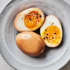 Trois œufs mariné soja, dont deux coupés en deux, révèlent un jaune d'œuf coulant et sont parsemés de graines de sésame.