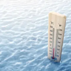 Drewniany termometr mierzy temperaturę wody na tle fal.