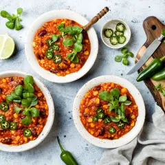Pyszne chili con carne wege w miseczkach, ozdobione zielonymi listkami i plasterkami jalapeño. Obok limonki i papryczki.