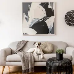 A dog lounges on a sofa, inspiring ideas on how to choose art for your home. Abstract art adorns the wall.