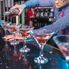 Barman nalewa różowy drink do kieliszków na barze.