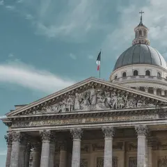 Majestatyczny Panteon w Paryżu z kopułą i francuską flagą na tle błękitnego nieba.
