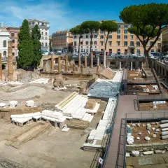 Antiche rovine dell'area sacra di Largo Argentina a Roma, con colonne e resti di templi sotto un cielo azzurro.