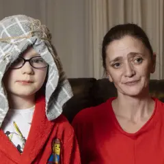Chłopiec w czerwonym szlafroku i ręczniku na głowie wygląda jak pastuszek. Obok siedzi kobieta.