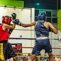 Two young boxers showcase their boxing skills in a ring, one in red, the other in blue, during a match.