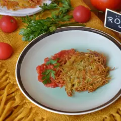 Chrupiące rosti ziemniaczane z pomidorami i natką pietruszki na talerzu, obok tabliczka z napisem "Rösti".
