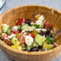 En härlig grekisk sallad med tomater, gurka, oliver och fetaost i en träskål.