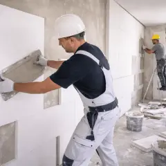 Operai applicano pannelli isolanti per creare un cappotto energetico, migliorando l'efficienza termica dell'edificio.