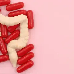 Model jelita otoczony czerwonymi kapsułkami, symbolizującymi leczenie, np. Pentasa.