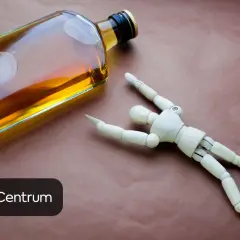Drewniany ludzik leży obok butelki alkoholu, symbolizując negatywny wpływ alkoholu na testosteron.