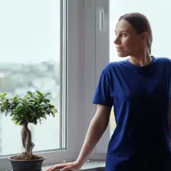 Kobieta wpatruje się w miasto przez okno, ciesząc się spokojem i pewnością, jaką daje gwarancja na okna.