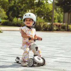 Uśmiechnięte dziecko w kasku na jeździku Scoot and Ride od kiedy zaczęło swoją przygodę z jazdą.