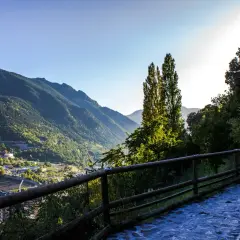 Sendero empedrado con barandilla de madera, vistas a un valle con edificios y montañas verdes. Ideal para explorar las **rutas Andorra**.