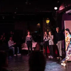 Publik applåderar en föreställning av improvisationsteater i Stockholm. Skådespelare på scenen tar emot hyllningar.