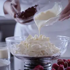 Kucharz wylewa płynną białą czekoladę na pokruszoną białą czekoladę, tworząc bazę do ganache z białej czekolady.