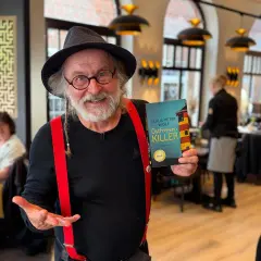 Klaus-Peter Wolf präsentiert "Ostfriesenkiller", Band 1 seiner Krimireihe. Ein Mann mit Hut und roten Hosenträgern hält das Buch hoch.