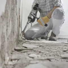 Un ouvrier utilise un marteau-piqueur pour démolir un mur. Des débris jonchent le sol. C'est une étape de travaux, comme dans une lettre d'information.