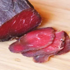 Kawałek ciemnoczerwonej bresaoli, z kilkoma cienkimi plastrami na drewnianej desce.