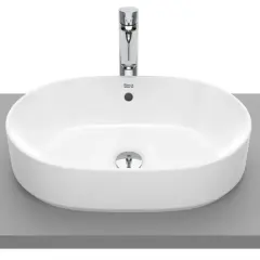 Elegancka, owalna umywalka nablatowa bez otworu na baterię, wykonana z białej ceramiki, z chromowanym korkiem.