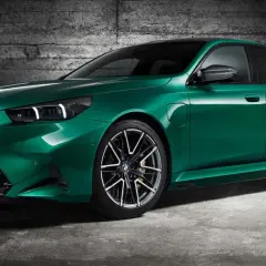 Zielony BMW M5 Competition z nowoczesnymi światłami i felgami stoi na tle betonowej ściany.