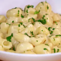 Mac and cheese cremoso, con trozos de perejil fresco espolvoreados. Un plato reconfortante y delicioso.