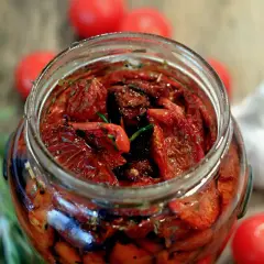Pomodori secchi sott'olio, la ricetta della nonna. Un barattolo pieno di sapore, con rosmarino e aglio sullo sfondo.