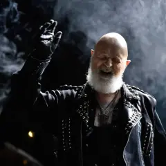 Rob Halford z Judas Priest, w skórzanej kurtce z ćwiekami, wznosi rękę w geście, jakby wykrzykując "Panic Attack" na koncercie.