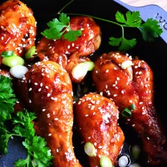 Kurczak teriyaki w glazurze z sezamem i szczypiorkiem w czarnej patelni.