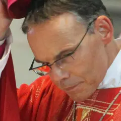 Bischof Tebartz van Elst trägt eine rote Messrobe und eine weiße Halskrause. Er blickt nach unten, während er eine Kopfbedeckung aufsetzt.