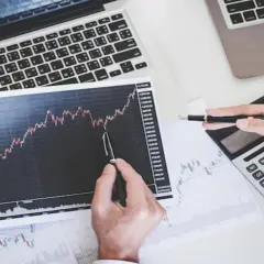 Analiza wykresu wzrostu akcji papiery wartościowe. Dłonie trzymają wykres i długopis, obok kalkulator i laptop.