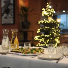 Stół wigilijny z przystawkami, napojami i ozdobioną choinką w tle. Zamówienia na wigilię w restauracji.