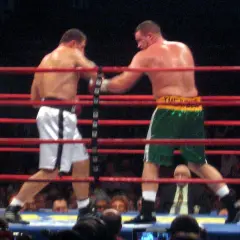Two boxers in a ring, one in white shorts, the other in green. This bout adheres to the light heavyweight boxing weight limit.