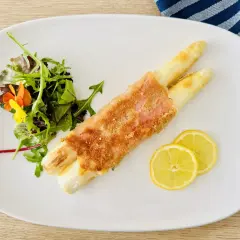 Spargel Cordon Bleu, knusprig paniert, serviert mit frischem Salat und Zitronenscheiben auf einem weißen Teller.