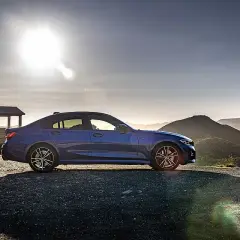 Niebieskie BMW 318d na tle górskiego krajobrazu o zachodzie słońca.