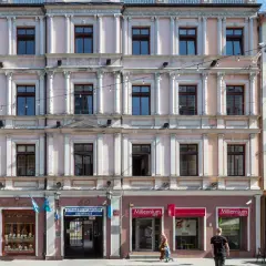 Kamienica przy ul. Piotrkowskiej 61 w Łodzi. Elegancka fasada z licznymi oknami i zdobieniami. Na parterze sklepy, m.in. jubiler i bank.