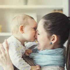 Ein süßer Moment zwischen Mutter und Baby (24 Wochen alt). Das Baby gibt der Mutter einen Nasenkuss, beide lächeln glücklich.